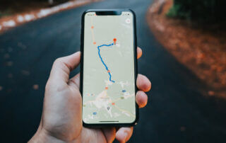Sur fond de route, une main tenant un téléphone cellulaire sur lequel est affiché un tracé sur une carte