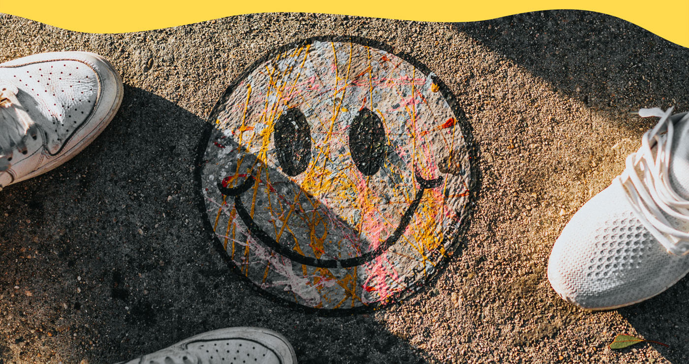 Icône de visage souriant (smiley) peint au sol entouré de trois souliers